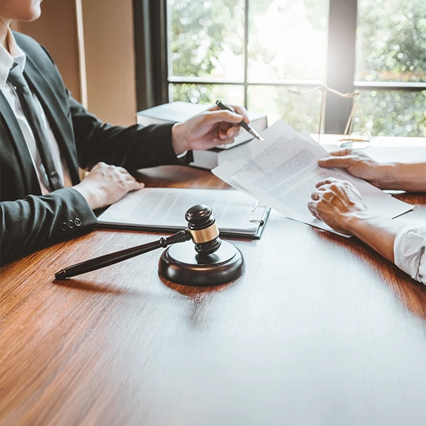 A lawyer in a suit reviewing contracts with a client at a wooden desk featuring a gavel and scales of justice, representing expert legal document services.